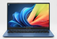 Asus Vivobook 15: Esta é uma imagem de estúdio, com estilo profissional. O notebook ASUS Vivobook 15 azul está aberto e posicionado de frente, centralizado sobre um fundo branco e minimalista. A iluminação é suave e uniforme, realçando o design elegante, a cor vibrante do aparelho e a sua tela ligada, que exibe um papel de parede colorido. A imagem transmite uma sensação de modernidade e sofisticação.