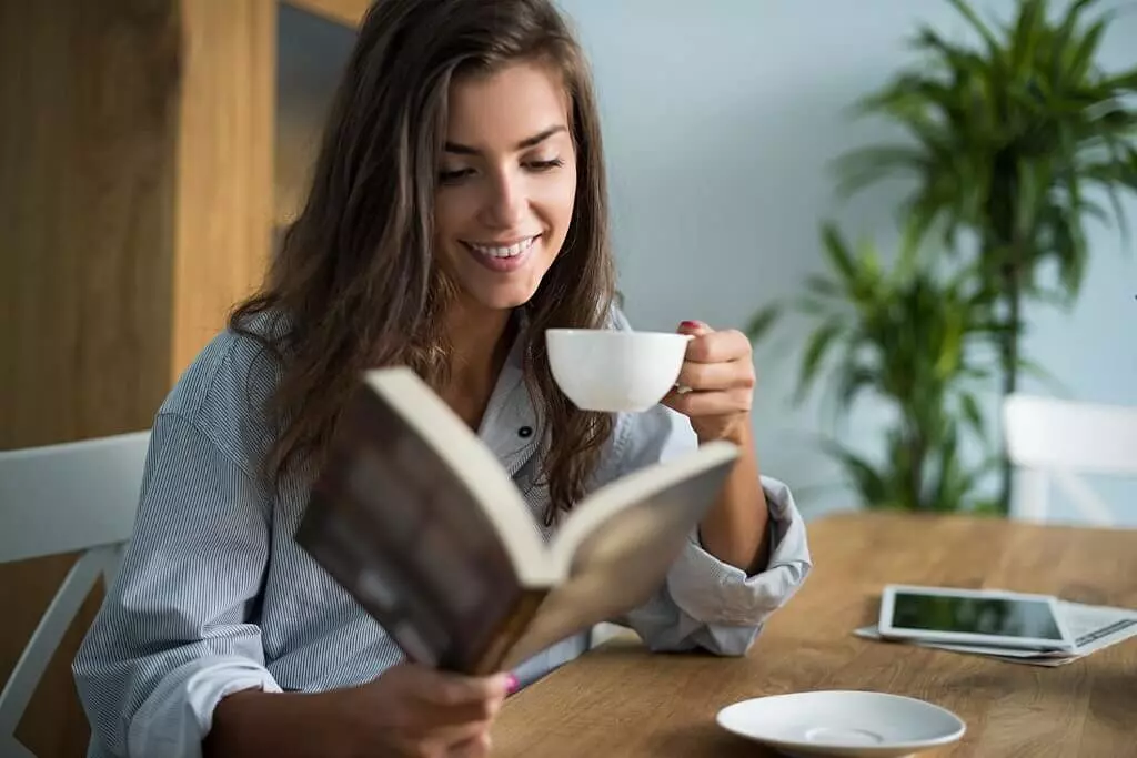 Como ganhar dinheiro escrevendo para web: Jovem leitora está a apreciar um bom livro enquanto toma um café. Crédito: GPoint Studio.