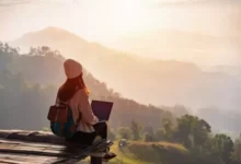 O que é Workation: Jovem mulher viajante freelancer trabalhando online em um workation, aproveitando a bela paisagem da natureza com vista para as montanhas ao nascer do sol. Crédito: Kitz Corner.