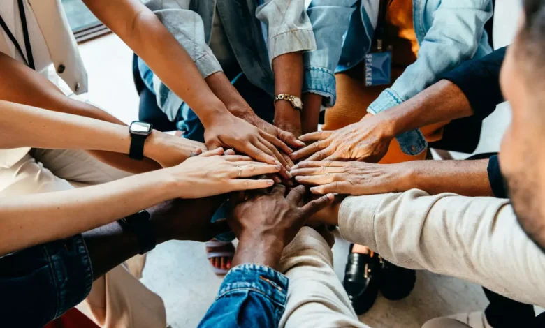 Dia do Amigo: Esta imagem mostra várias pessoas unindo as mãos no centro, formando um círculo de braços. A foto foi tirada de cima, destacando a diversidade dos participantes e simbolizando união, apoio mútuo e trabalho em equipe. As mãos juntas transmitem uma forte mensagem de conexão, solidariedade e amizade, tornando a imagem perfeita para ilustrar temas como colaboração, confiança, inclusão e o valor dos laços entre amigos ou colegas. Crédito: iStock.