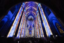 Interior da Catedral da Sé iluminado por projeções em tons de azul e dourado que cobrem colunas e abóbadas góticas durante o espetáculo LuminiScence.