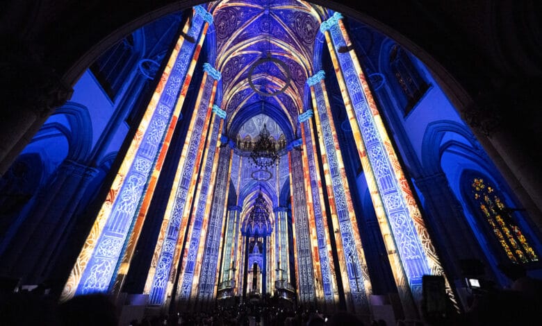 Interior da Catedral da Sé iluminado por projeções em tons de azul e dourado que cobrem colunas e abóbadas góticas durante o espetáculo LuminiScence.