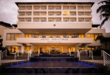 Fachada do Hotel Jequitimar Resort & Spa iluminada ao entardecer, com escadarias, espelho d’água e palmeiras ao redor.