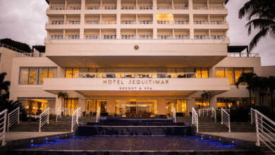 Fachada do Hotel Jequitimar Resort & Spa iluminada ao entardecer, com escadarias, espelho d’água e palmeiras ao redor.