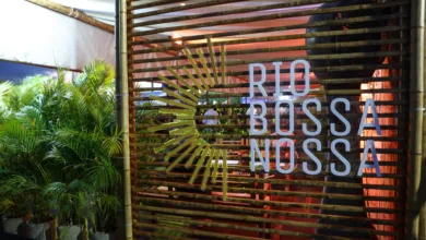 Entrada do festival Rio Bossa Nossa com estrutura de madeira, identidade visual do evento e plantas decorativas ao redor.