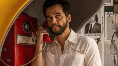 Wagner Moura em cena do filme O Agente Secreto, usando telefone público em ambiente urbano.