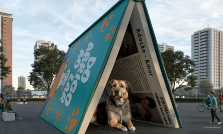 Instalação artística em formato de livro aberto formando um abrigo, com um cachorro deitado em seu interior, em espaço público próximo ao Ibirapuera.