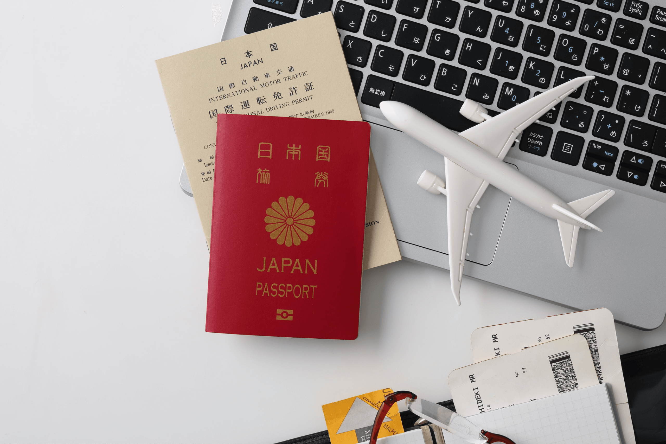 Passaporte japonês, passagens aéreas e avião em miniatura sobre um notebook.