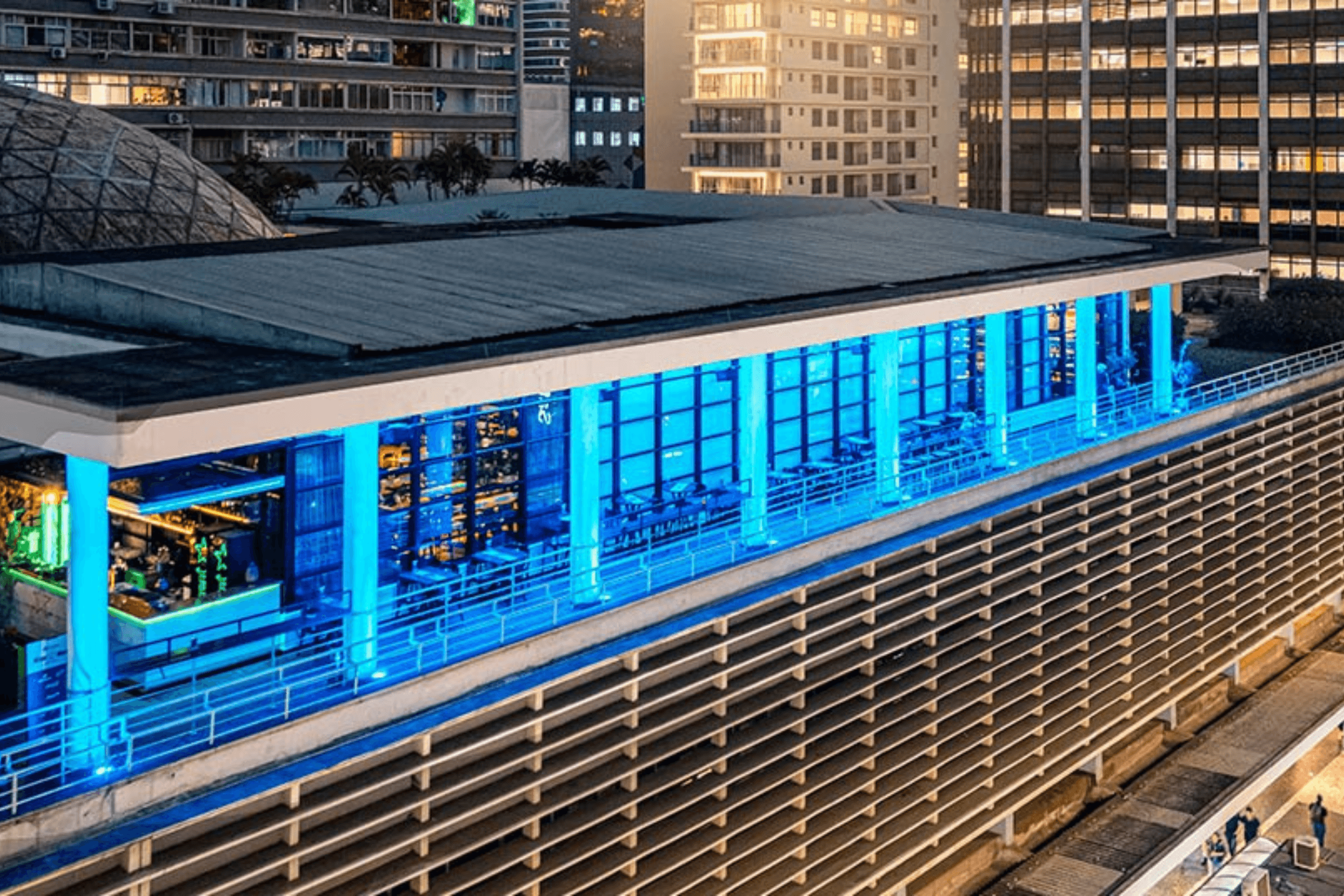 Fachada do Blue Note São Paulo iluminada em azul durante a noite, com prédios ao fundo.