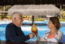 Casal de idosos brinda com drinques em bar dentro da piscina de um resort.
