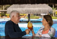 Casal de idosos brinda com drinques em bar dentro da piscina de um resort.