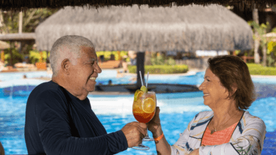 Casal de idosos brinda com drinques em bar dentro da piscina de um resort.