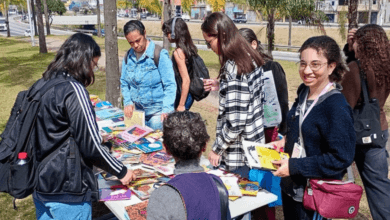 Pessoas reunidas ao redor de uma mesa escolhem livros durante feira de doação em área externa.