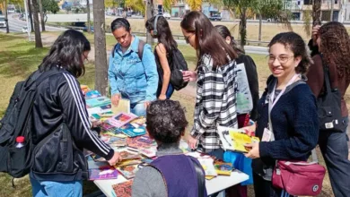 Pessoas reunidas ao redor de uma mesa escolhem livros durante feira de doação em área externa.