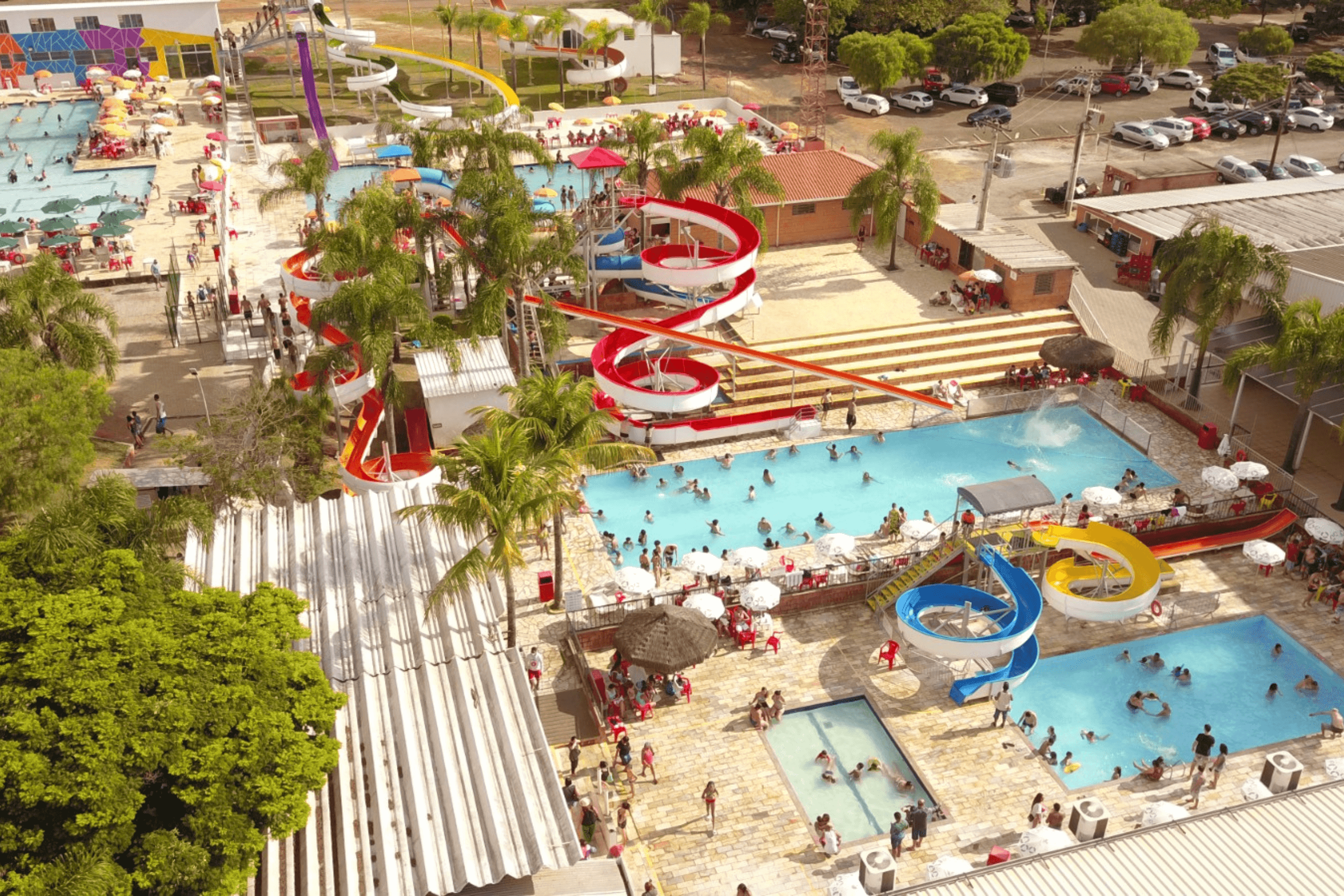 Vista aérea do parque aquático da Pousada Maeda com piscinas repletas de banhistas e diversos toboáguas coloridos em espiral.