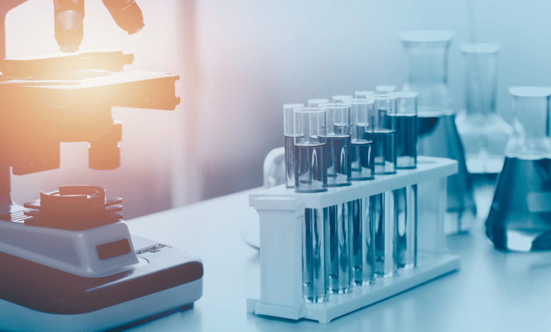 Microscópio e rack com tubos de ensaio em laboratório de controle de qualidade.