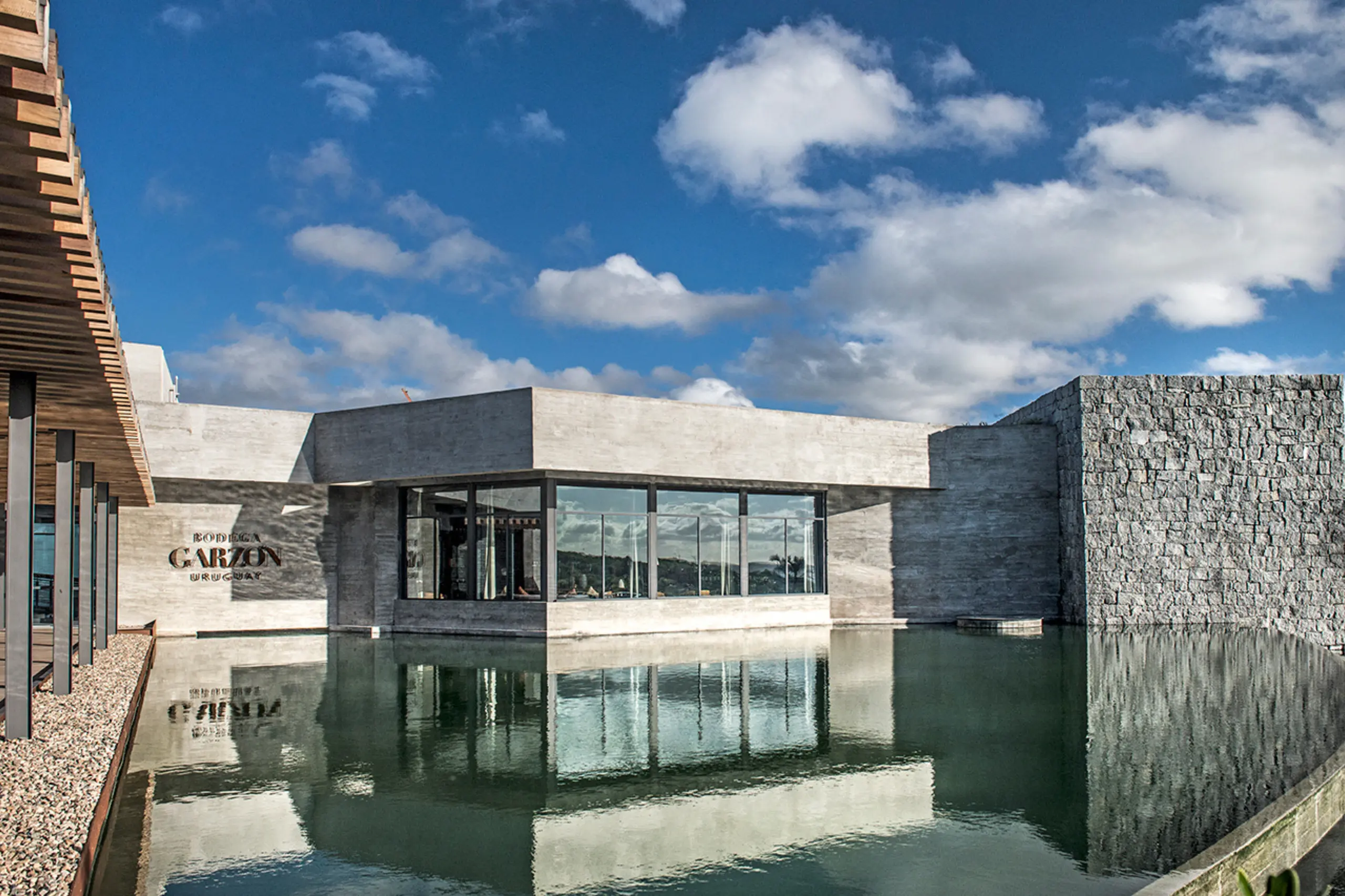 Fachada contemporânea da Bodega Garzón com espelho d'água refletindo a estrutura de concreto e madeira, vinícola uruguaia próxima a Punta del Este