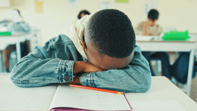 Criança com a cabeça apoiada sobre o caderno na sala de aula, ilustrando a sonolência diurna e o cansaço por falta de sono.