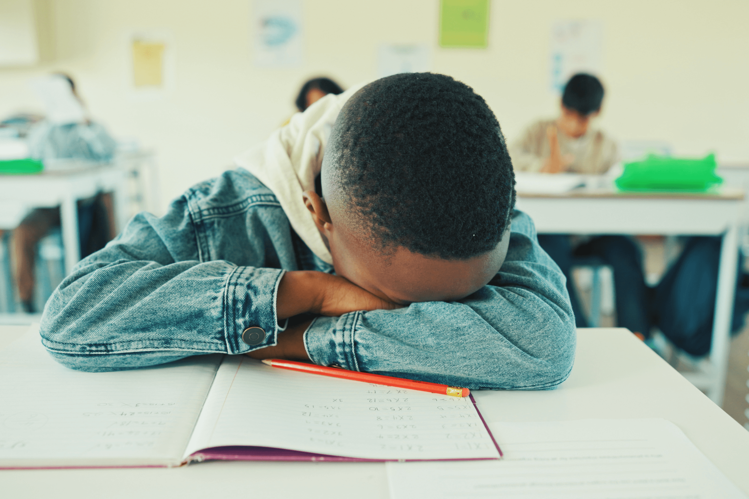 Criança com a cabeça apoiada sobre o caderno na sala de aula, ilustrando a sonolência diurna e o cansaço por falta de sono.