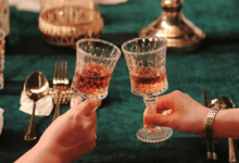 Close de duas pessoas brindando com taças em uma mesa de restaurante elegante com iluminação quente.