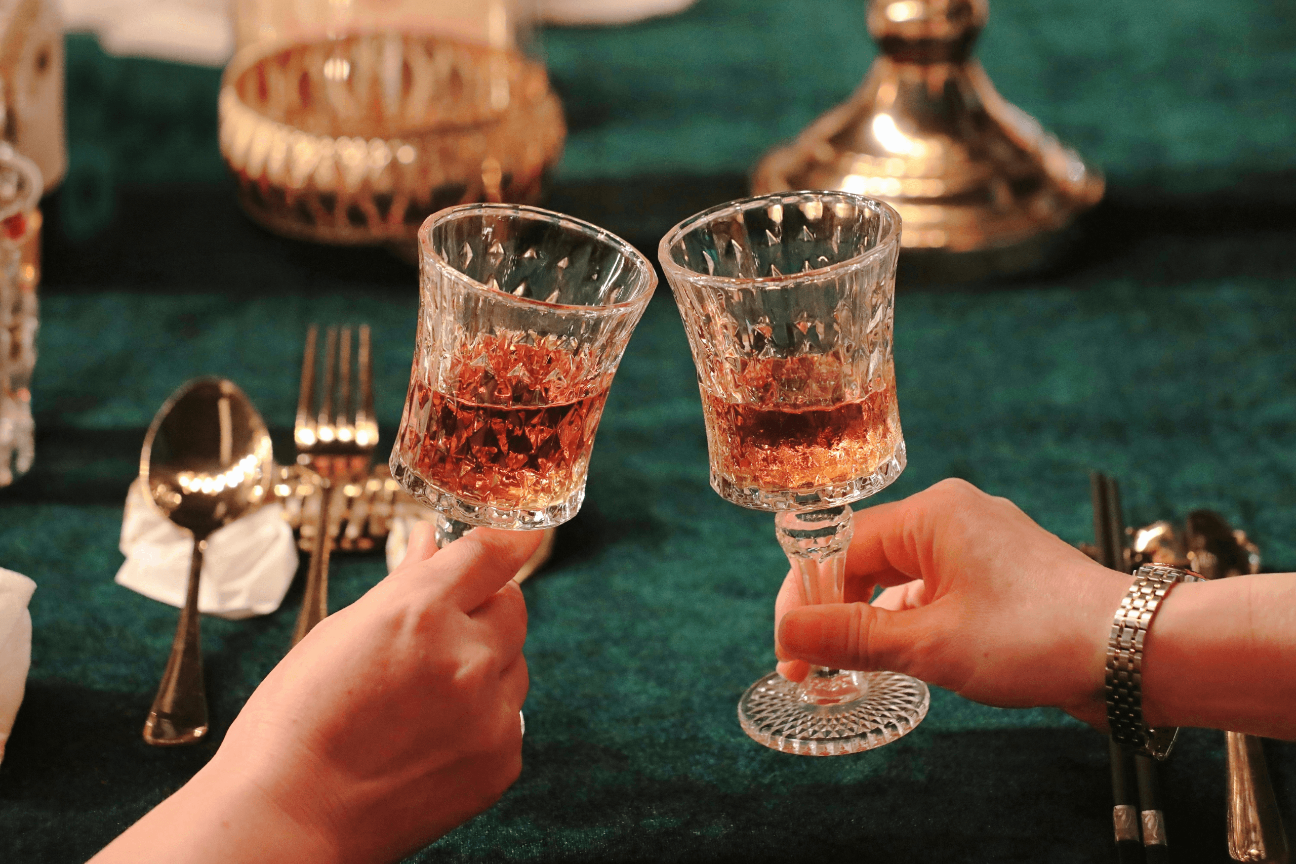 Close de duas pessoas brindando com taças em uma mesa de restaurante elegante com iluminação quente.