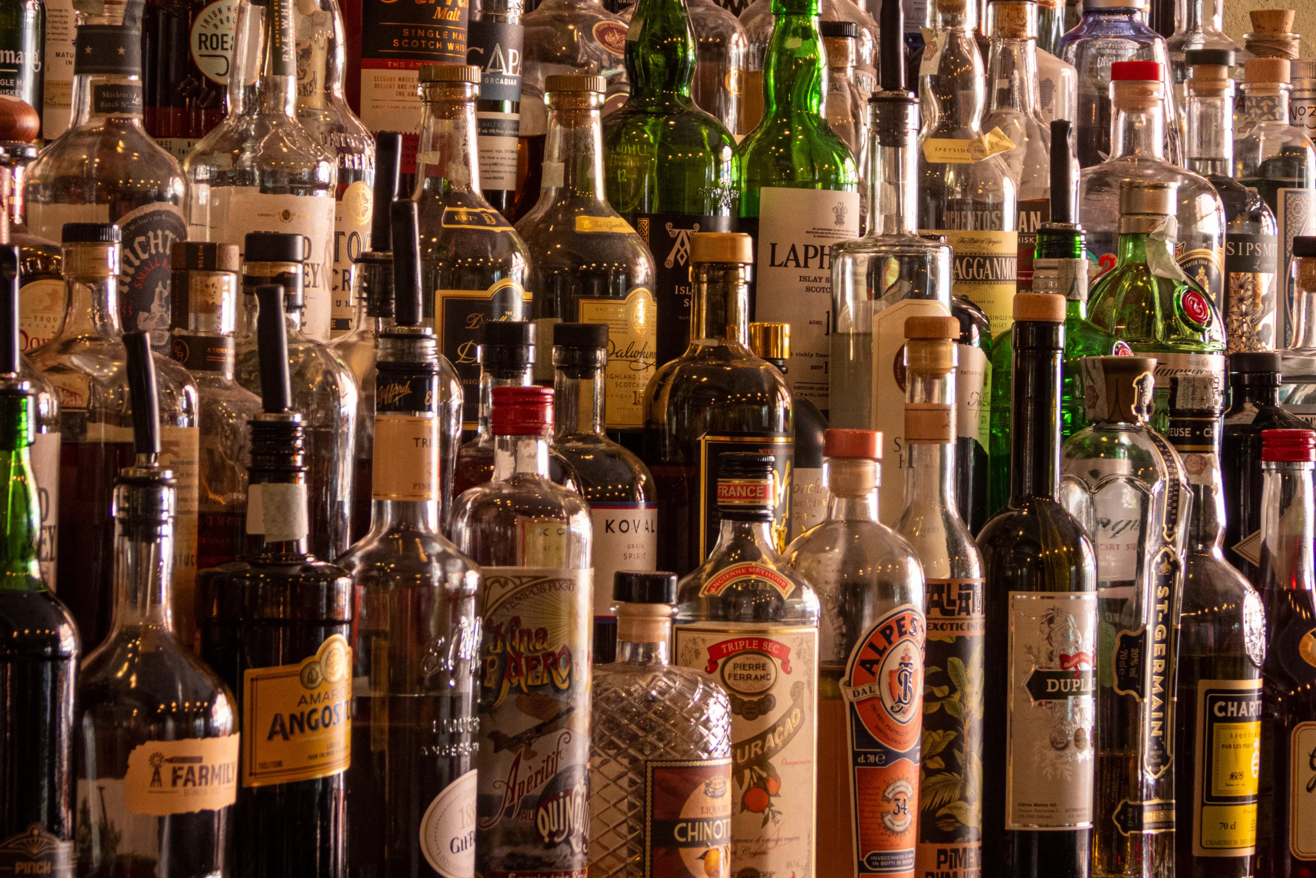 Prateleira repleta de garrafas de bebidas alcoólicas variadas como gins, licores e uísques.