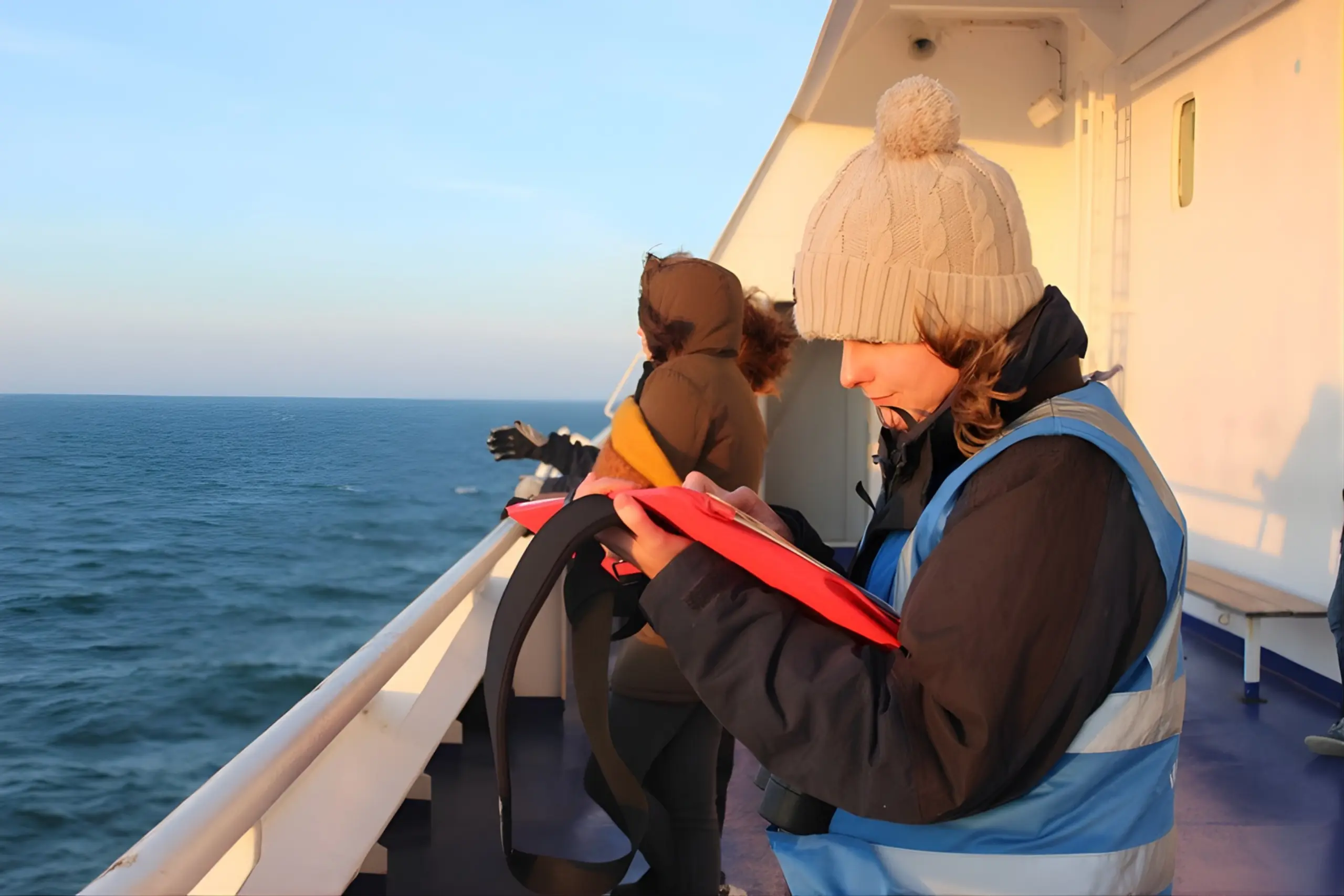 Observadora de Mamíferos Marinhos da ORCA registrando dados no convés de navio com o oceano ao fundo