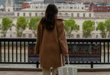 Mulher de costas segurando uma mala de viagem diante de uma paisagem urbana com rio, simbolizando liberdade e descanso.