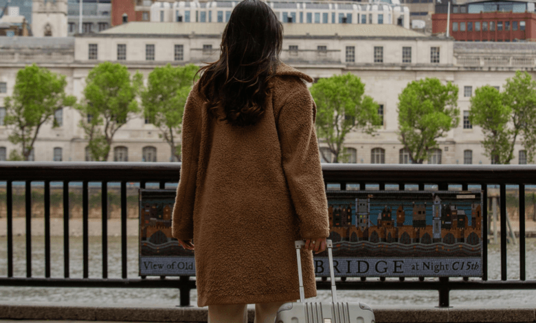 Mulher de costas segurando uma mala de viagem diante de uma paisagem urbana com rio, simbolizando liberdade e descanso.