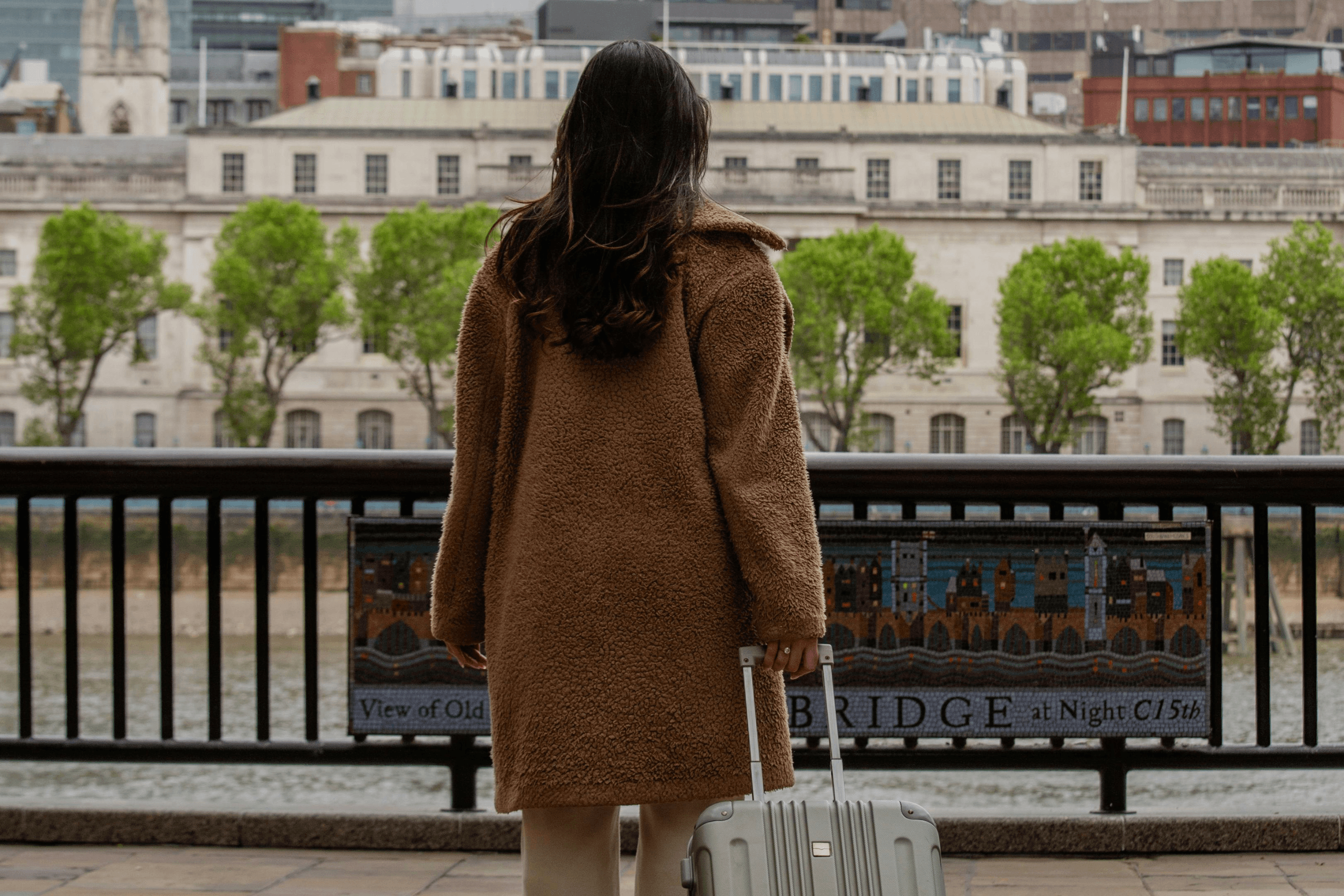 Mulher de costas segurando uma mala de viagem diante de uma paisagem urbana com rio, simbolizando liberdade e descanso.