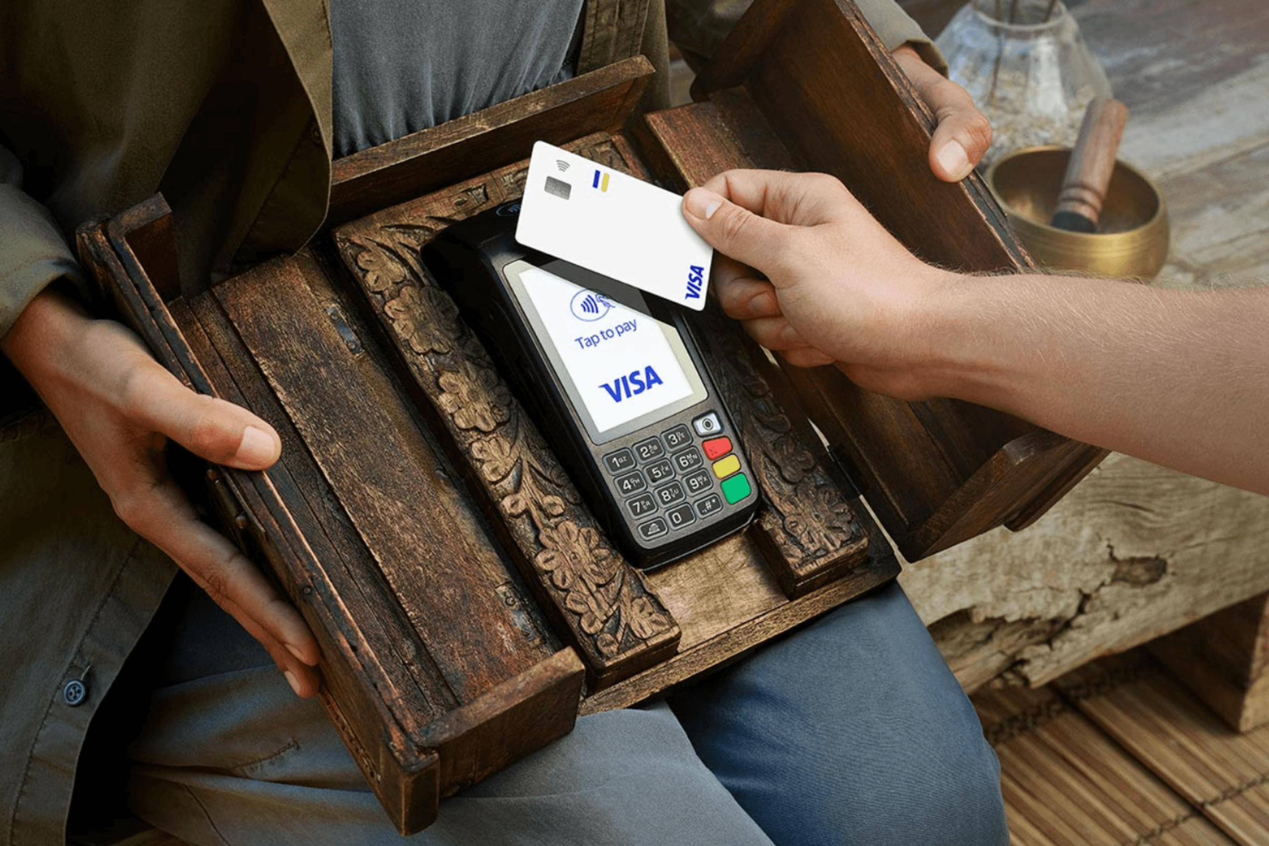 Close-up de uma mão aproximando um cartão de crédito branco de uma máquina de pagamento Visa para realizar uma transação sem contato.