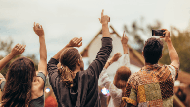 Vista de costas de um grupo de jovens com braços levantados celebrando em um festival de música ao ar livre.