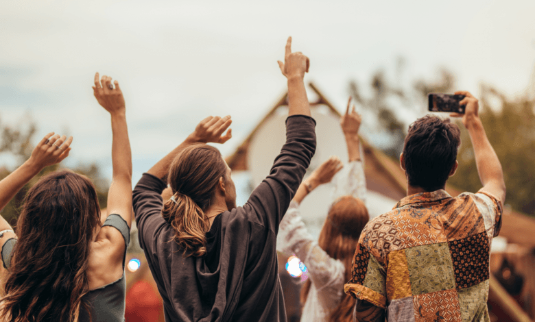 Vista de costas de um grupo de jovens com braços levantados celebrando em um festival de música ao ar livre.