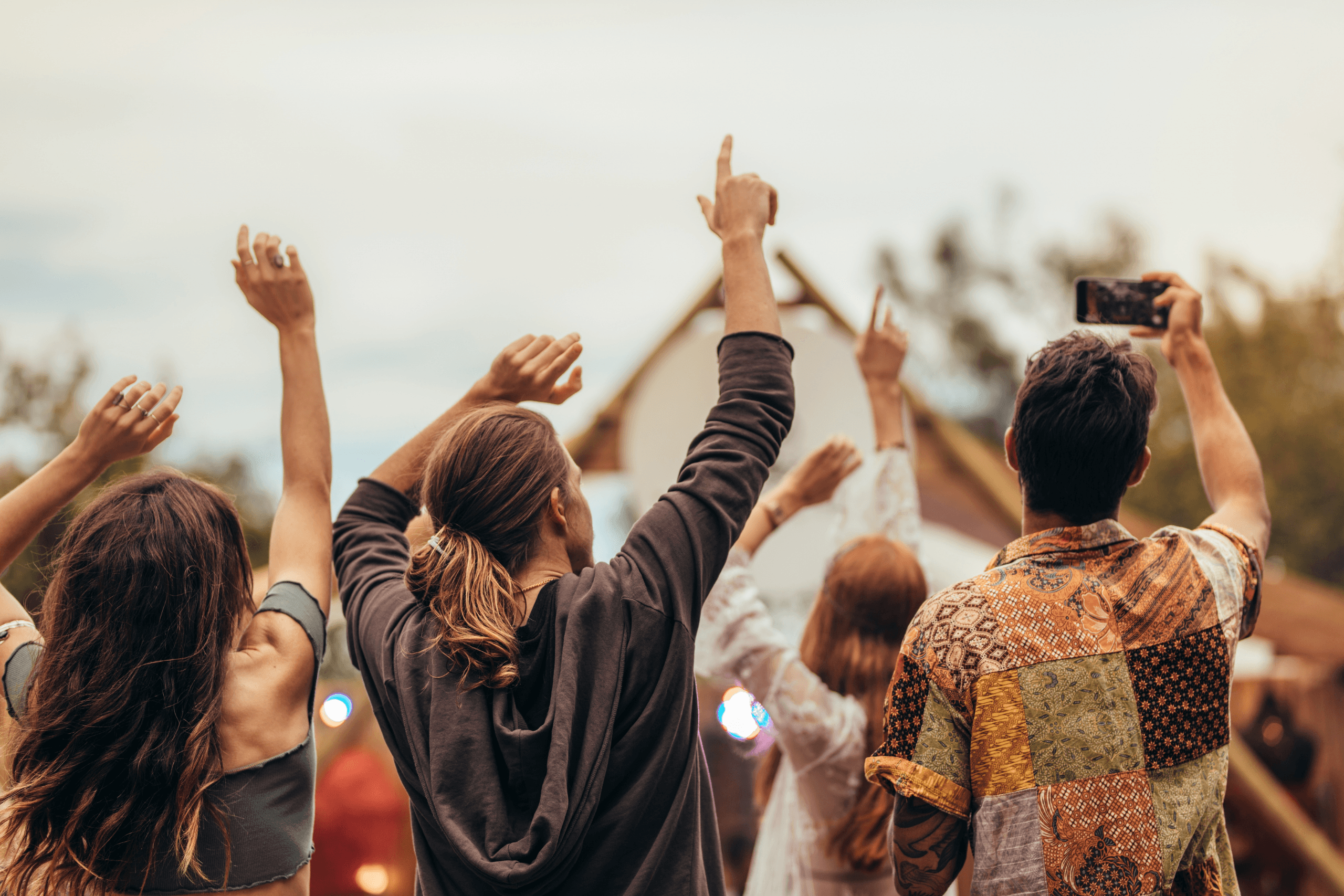 Vista de costas de um grupo de jovens com braços levantados celebrando em um festival de música ao ar livre.