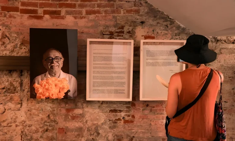 Visitante observando exposição com retrato de Gabriel García Márquez e manuscritos emoldurados em parede de tijolos na Colômbia
