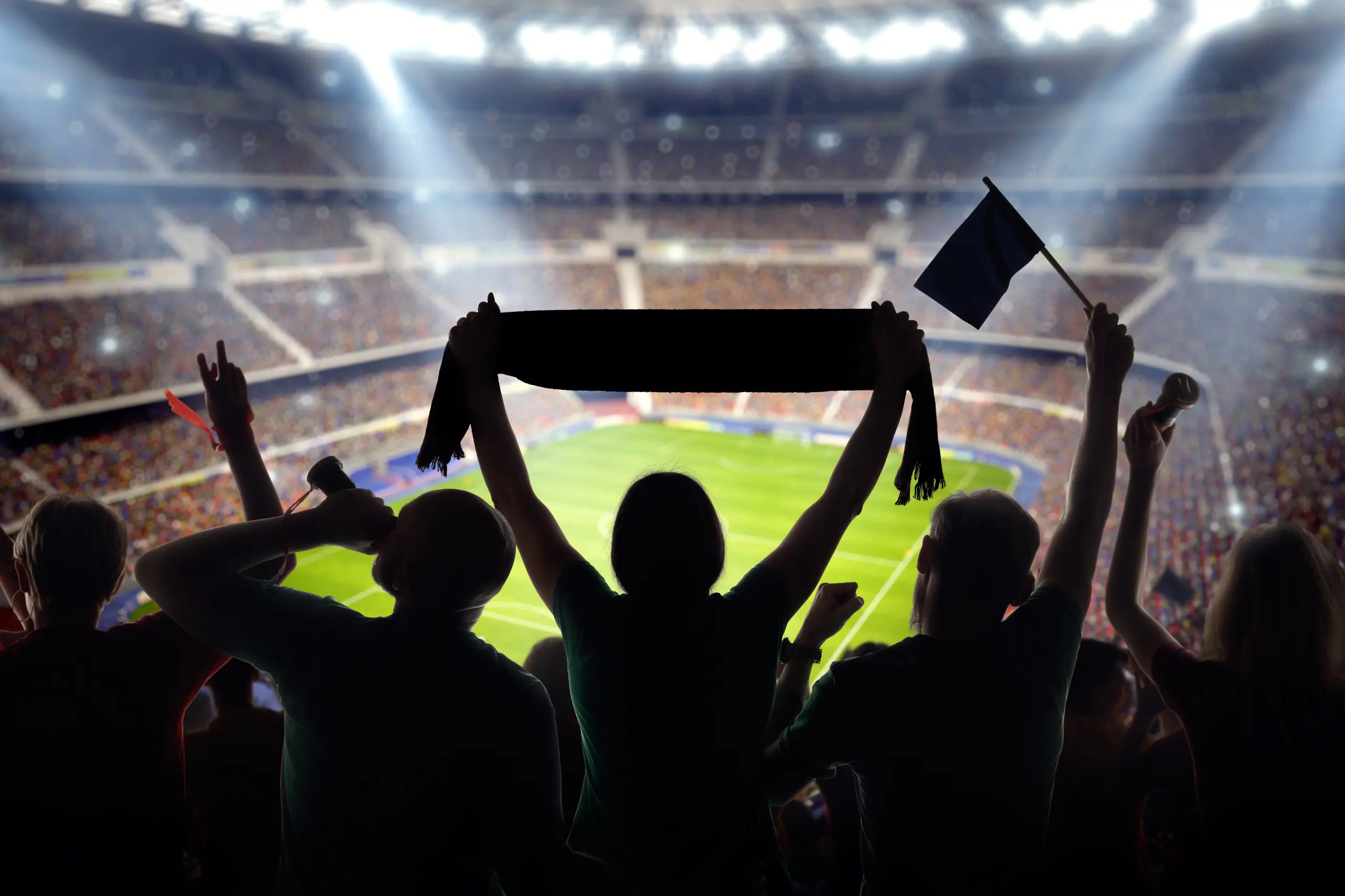 Silhueta de torcedores celebrando dentro de estádio iluminado durante jogo de futebol.