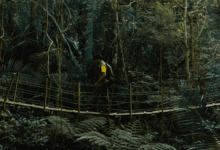 Viajante com mochila atravessando ponte suspensa de madeira em meio à vegetação densa da Trilha Caminhos da Ibiapaba