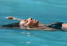 Mulher de olhos fechados flutuando relaxada em piscina de água termal azul-turquesa