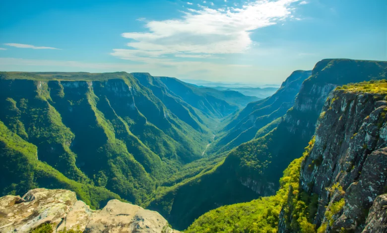 Vista panorâmica de um cânion profundo com paredões de rocha cobertos por vegetação verde sob um céu azul com nuvens esparsas.