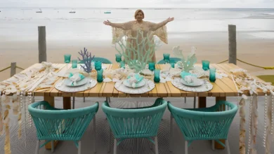 Martha Medeiros de braços abertos atrás de mesa decorada com elementos marinhos na praia de Milagres em Alagoas