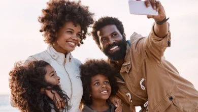 Família negra sorrindo tirando selfie em passeio ao ar livre com céu claro ao fundo