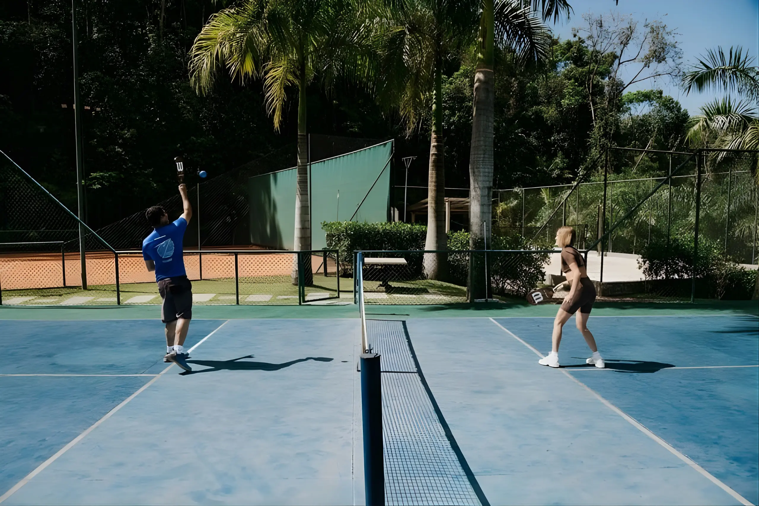 Dois jogadores praticando pickleball em quadra do Rituaali Clínica & Spa rodeada por palmeiras e vegetação tropical