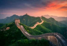 Vista aérea da Grande Muralha da China serpenteando por montanhas verdes ao entardecer com céu em tons de laranja e roxo