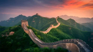 Vista aérea da Grande Muralha da China serpenteando por montanhas verdes ao entardecer com céu em tons de laranja e roxo