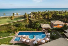 Vista aérea do Hotel Boutique e Spa Ponta de Inhambupe com piscina, palmeiras e o mar ao fundo em dia ensolarado