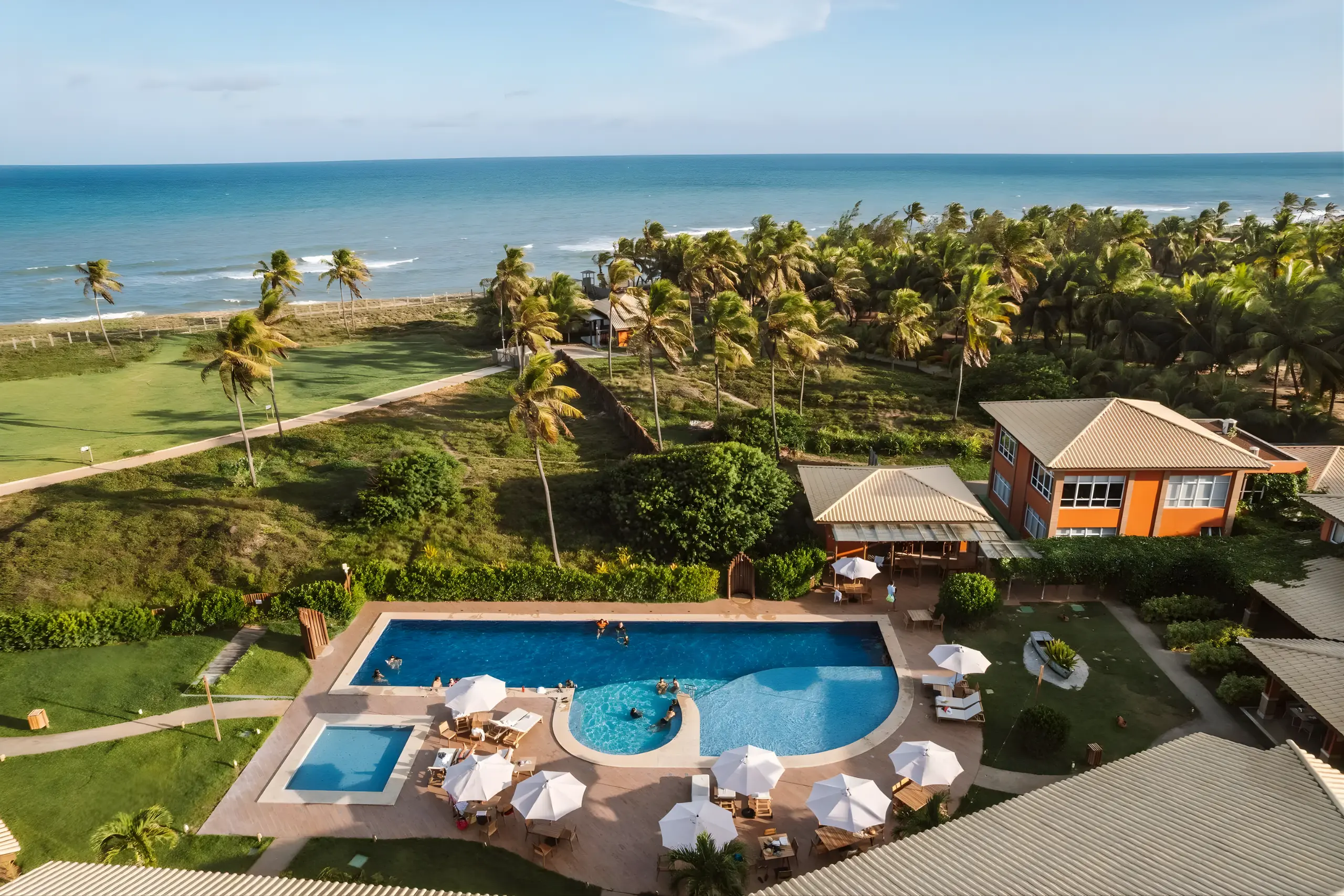 Vista aérea do Hotel Boutique e Spa Ponta de Inhambupe com piscina, palmeiras e o mar ao fundo em dia ensolarado