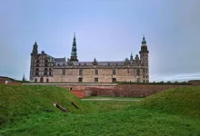 Vista frontal do Kronborg Castle em Helsingør na Dinamarca com muralhas de grama verde e torres com cúpulas verdes sob céu nublado