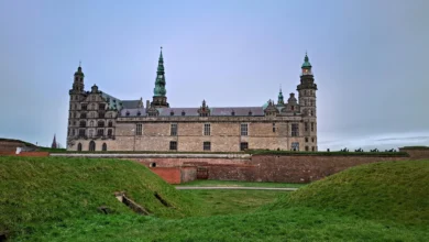 Vista frontal do Kronborg Castle em Helsingør na Dinamarca com muralhas de grama verde e torres com cúpulas verdes sob céu nublado