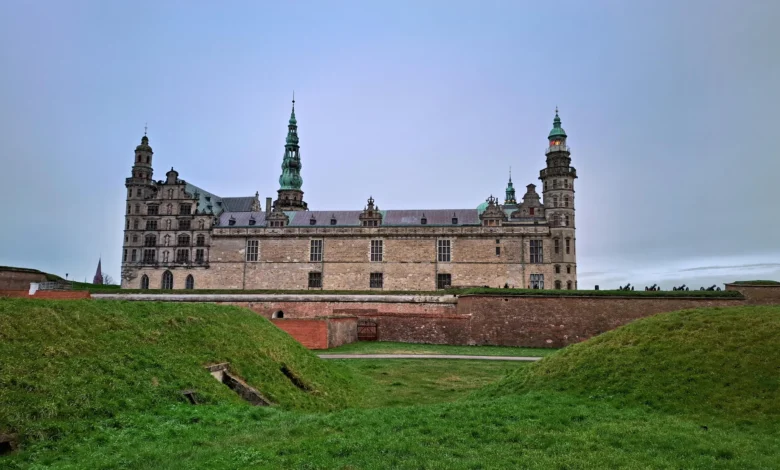 Vista frontal do Kronborg Castle em Helsingør na Dinamarca com muralhas de grama verde e torres com cúpulas verdes sob céu nublado