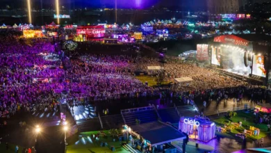 Vista aérea noturna do Lollapalooza Brasil no Autódromo de Interlagos com multidão e palco iluminado em tons de roxo e laranja